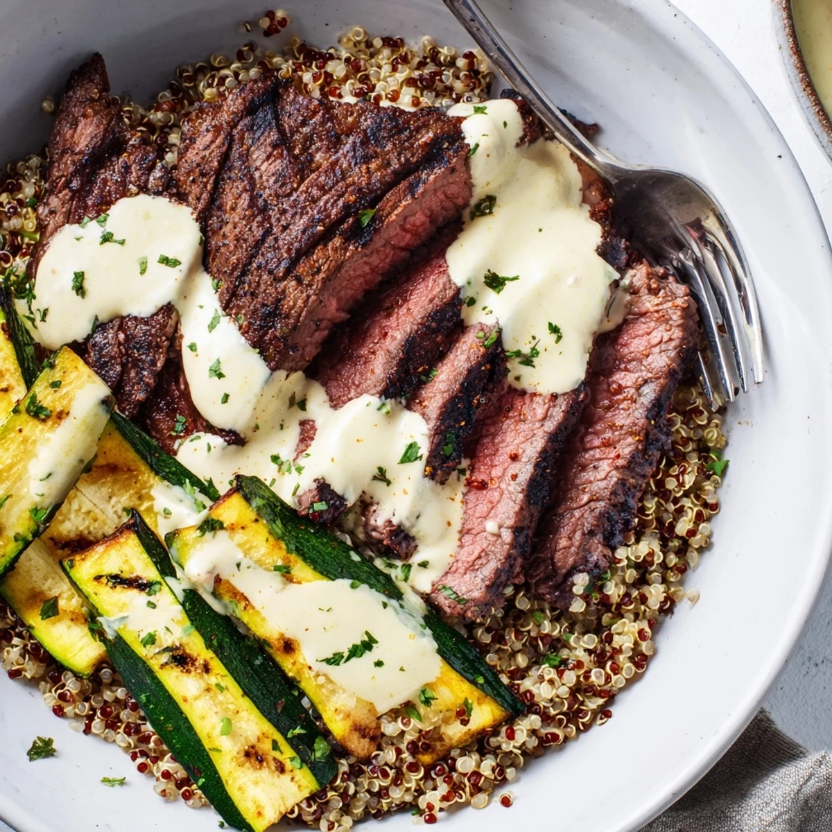 Tender steak slices on fluffy quinoa with smoky grilled zucchini and garlic cream sauce.  