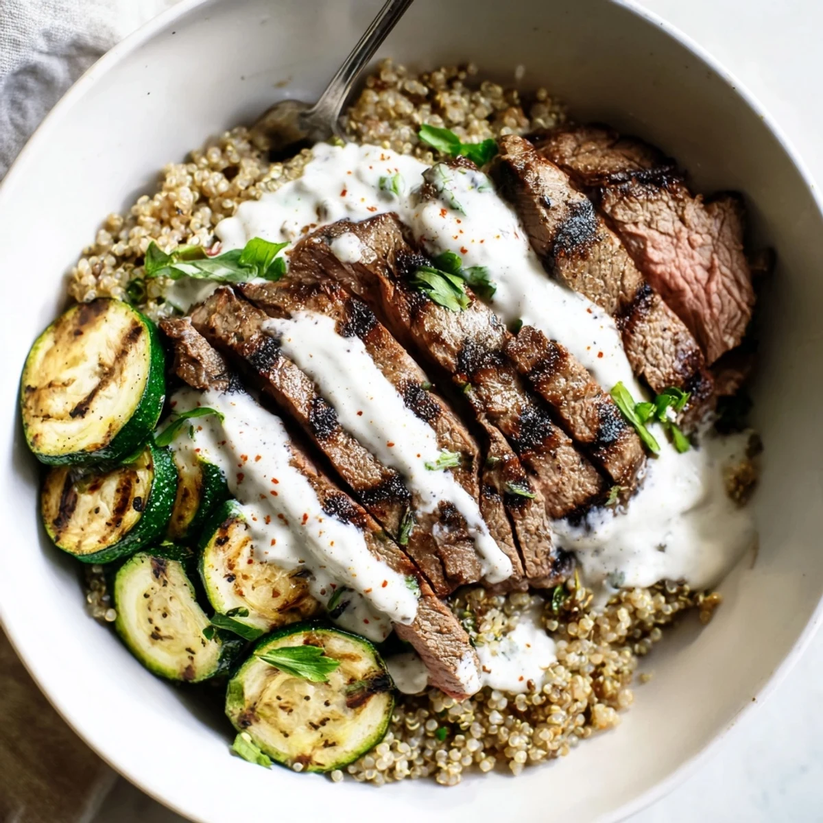 Colorful grilled steak bowl featuring creamy sauce, quinoa, and perfectly charred zucchini.