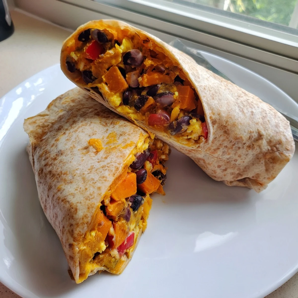 Perfectly wrapped sweet potato and black bean breakfast burritos ready to enjoy with a cheesy filling.