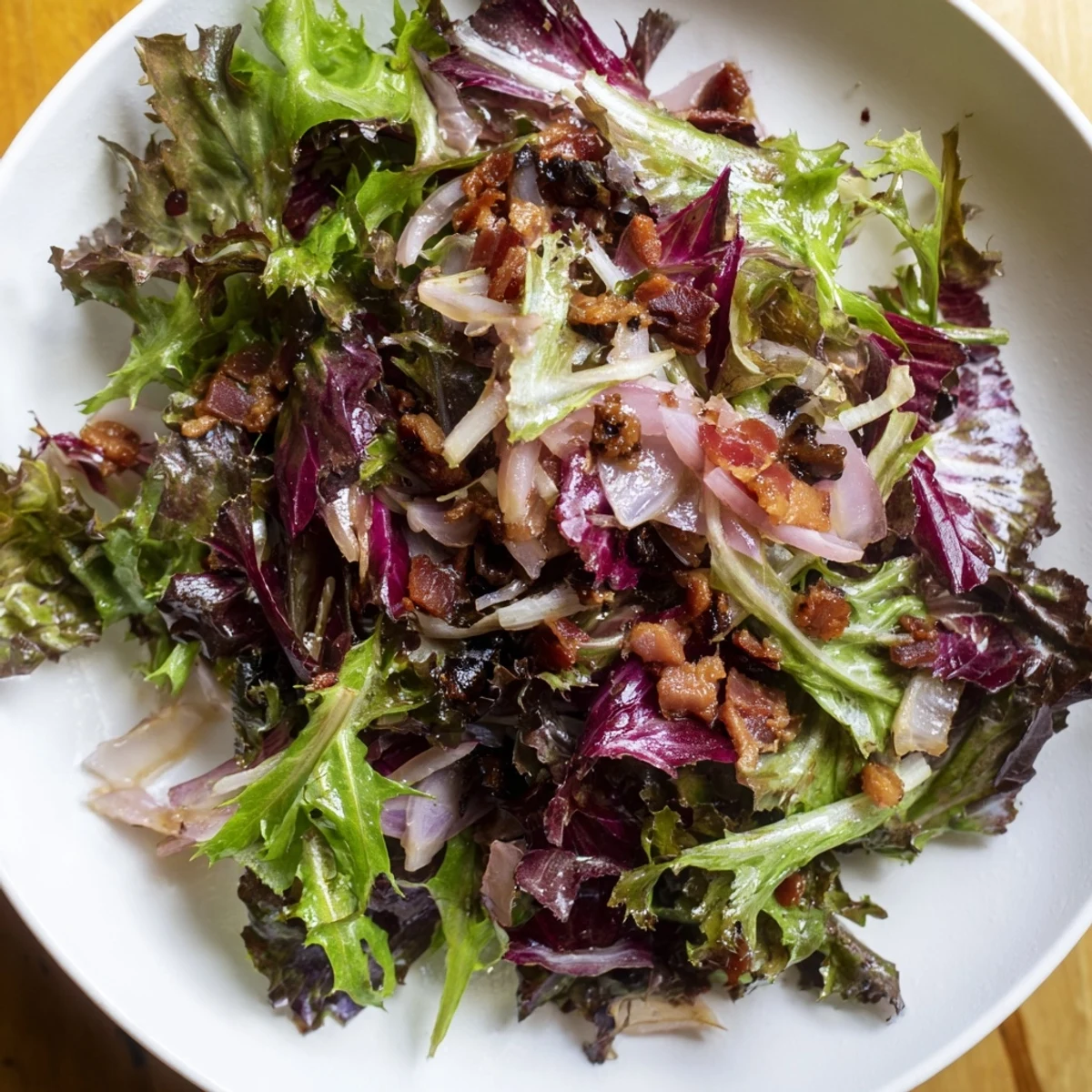 A flavorful Bitter Greens Salad with Warm Bacon Dressing, served warm with crispy bacon crumbles.