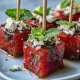 Colorful watermelon and feta skewers arranged on a platter, garnished with mint leaves and a sprinkle of black pepper for a fresh appetizer.  