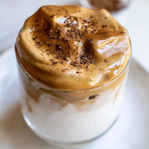 A luscious Brown Sugar Dalgona Latte topped with whipped coffee, swirled over cold milk and ice.