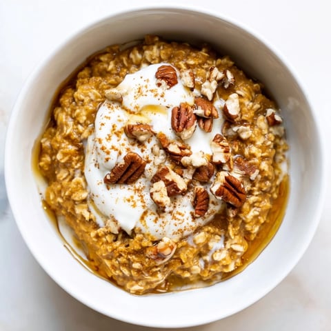 Steaming bowl of pumpkin spice latte oats topped with pecans and a swirl of whipped cream.