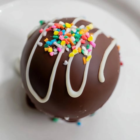 Steaming mug reveals a melting, decadent Hot Chocolate Bomb surrounded by snowy marshmallows.
