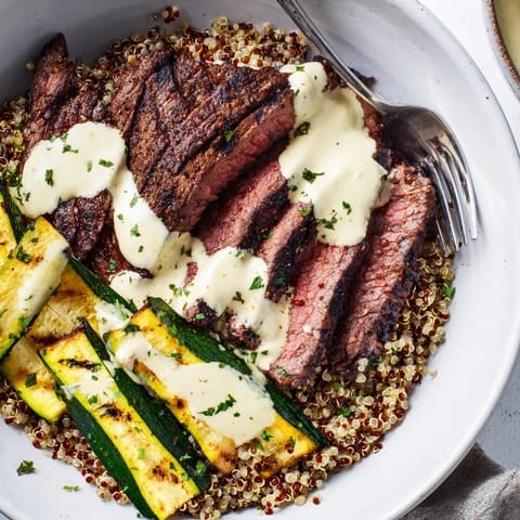 Tender steak slices on fluffy quinoa with smoky grilled zucchini and garlic cream sauce.  