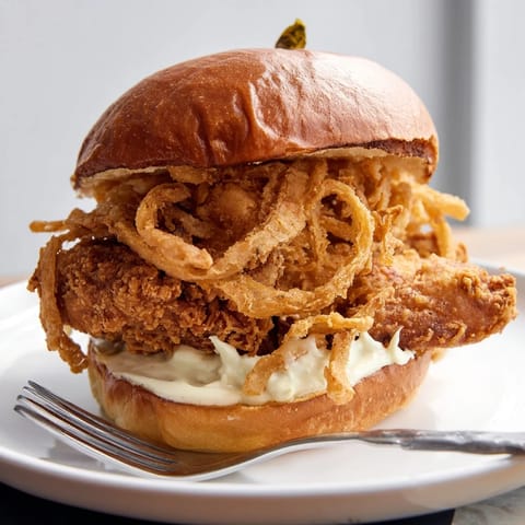 A close-up of the Crispy Onion Chicken Sandwich showing juicy buttermilk chicken, crunchy onion strings, and melted butter on the soft bun.