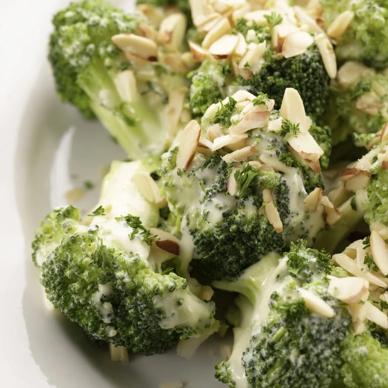 Garlic Parmesan Broccoli Salad served in a white bowl with red onion slices and cherry tomatoes.